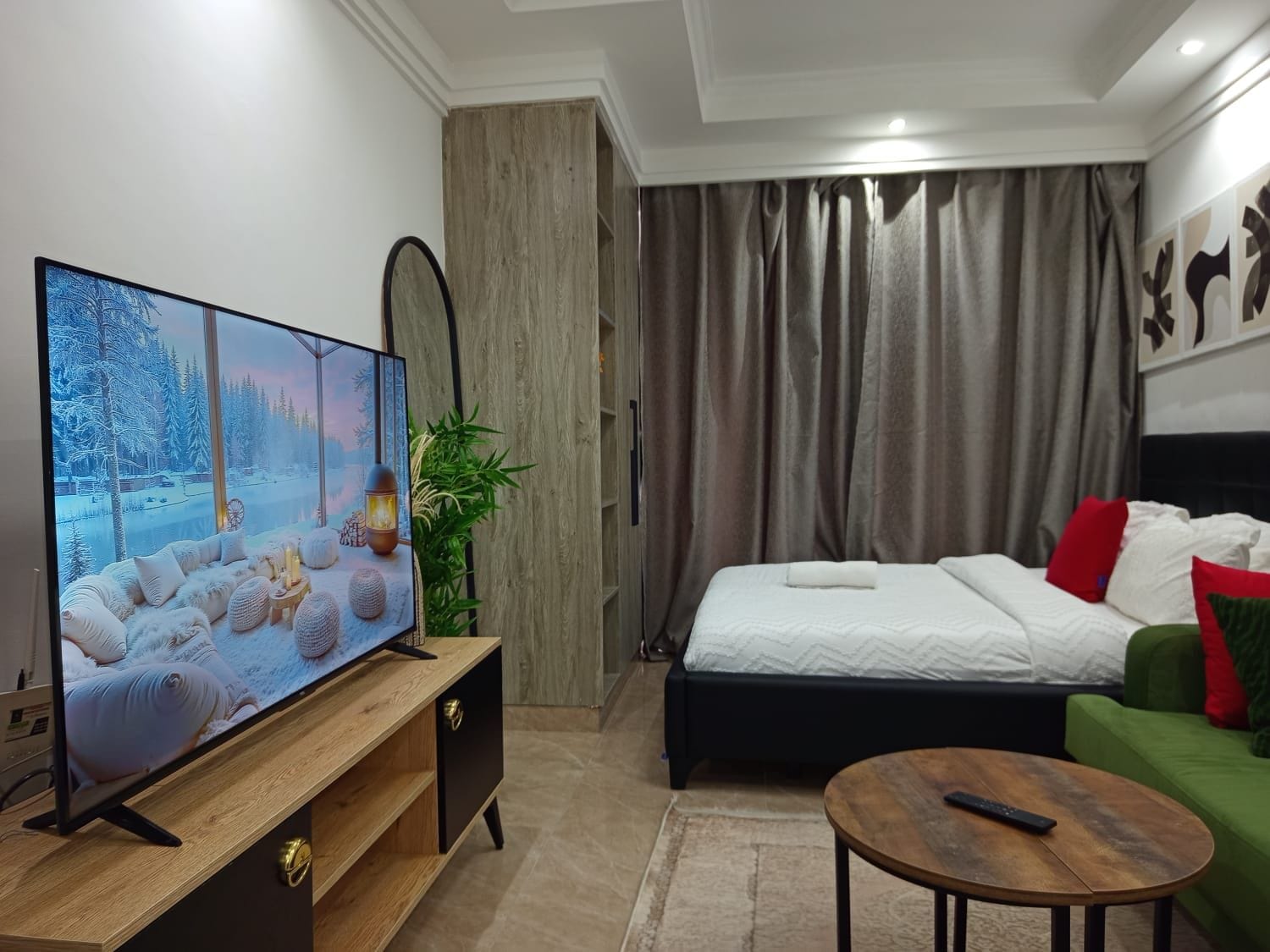 Una habitación de hotel moderna con un televisor de pantalla plana grande, una cama con ropa blanca, un sofá verde y una mesa de centro de madera.