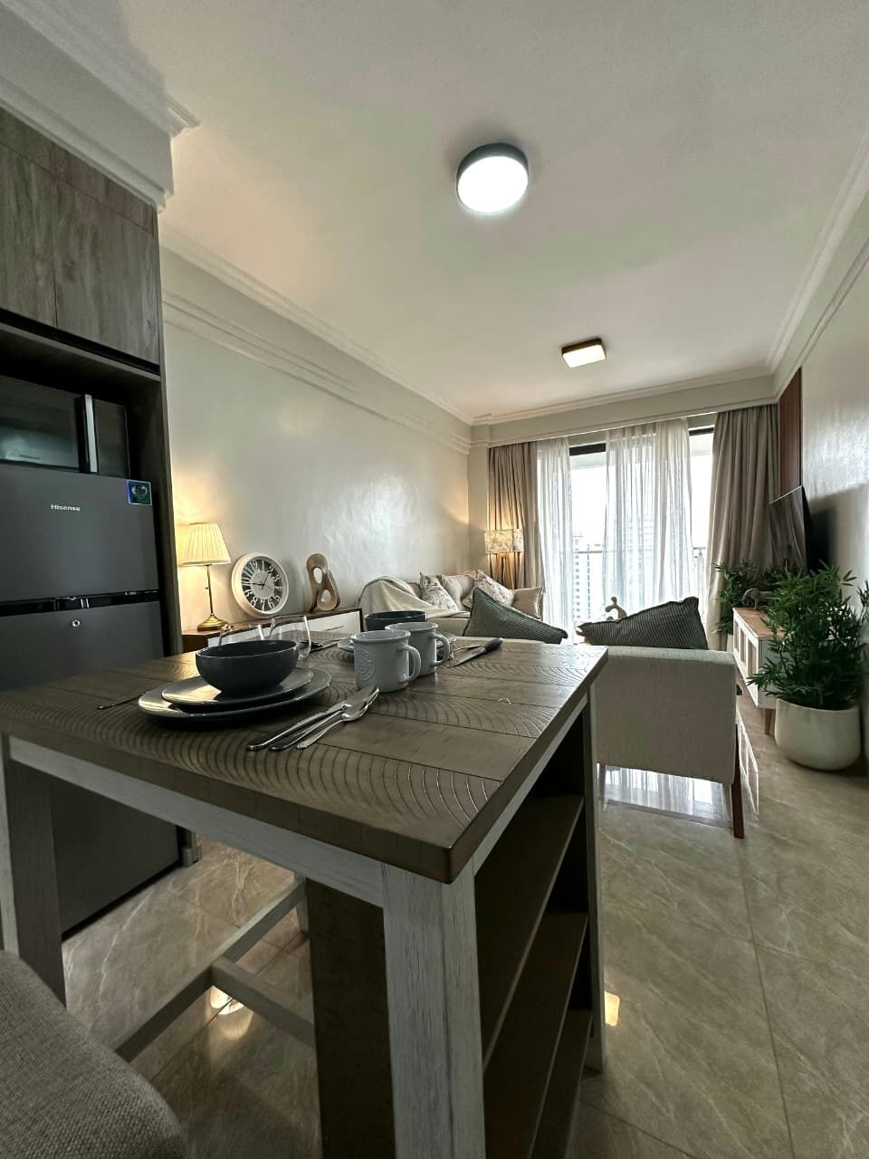 A modern kitchen with a dining area, a refrigerator, a clock, and a plant.