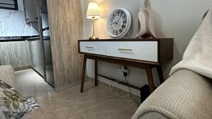 A living room with a sofa, a side table with a lamp, a clock, and a wall-mounted shelf. - Padmore Residences Kilimani (Nairobi)