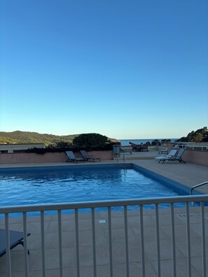Uma piscina com espreguiçadeiras e vista para o mar.