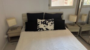 A bedroom with a large bed, two bedside tables with lamps, a window with a view of buildings, and a patterned bedspread. - Vacation Apartment (La Croix-Valmer)