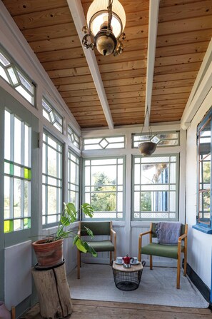 A sunroom with wooden beams, large windows, and a hanging light fixture.