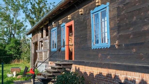 A wooden house with a red door and blue window frames, a staircase leading to the entrance, and a brick foundation. - Dom Dobrego Lata – Historic House in Drewnica (Drewnica)