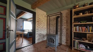 A room with a brick wall, a wooden floor, a blue sofa, a bookshelf, and a vintage stove. - Dom Dobrego Lata – Historic House in Drewnica (Drewnica)