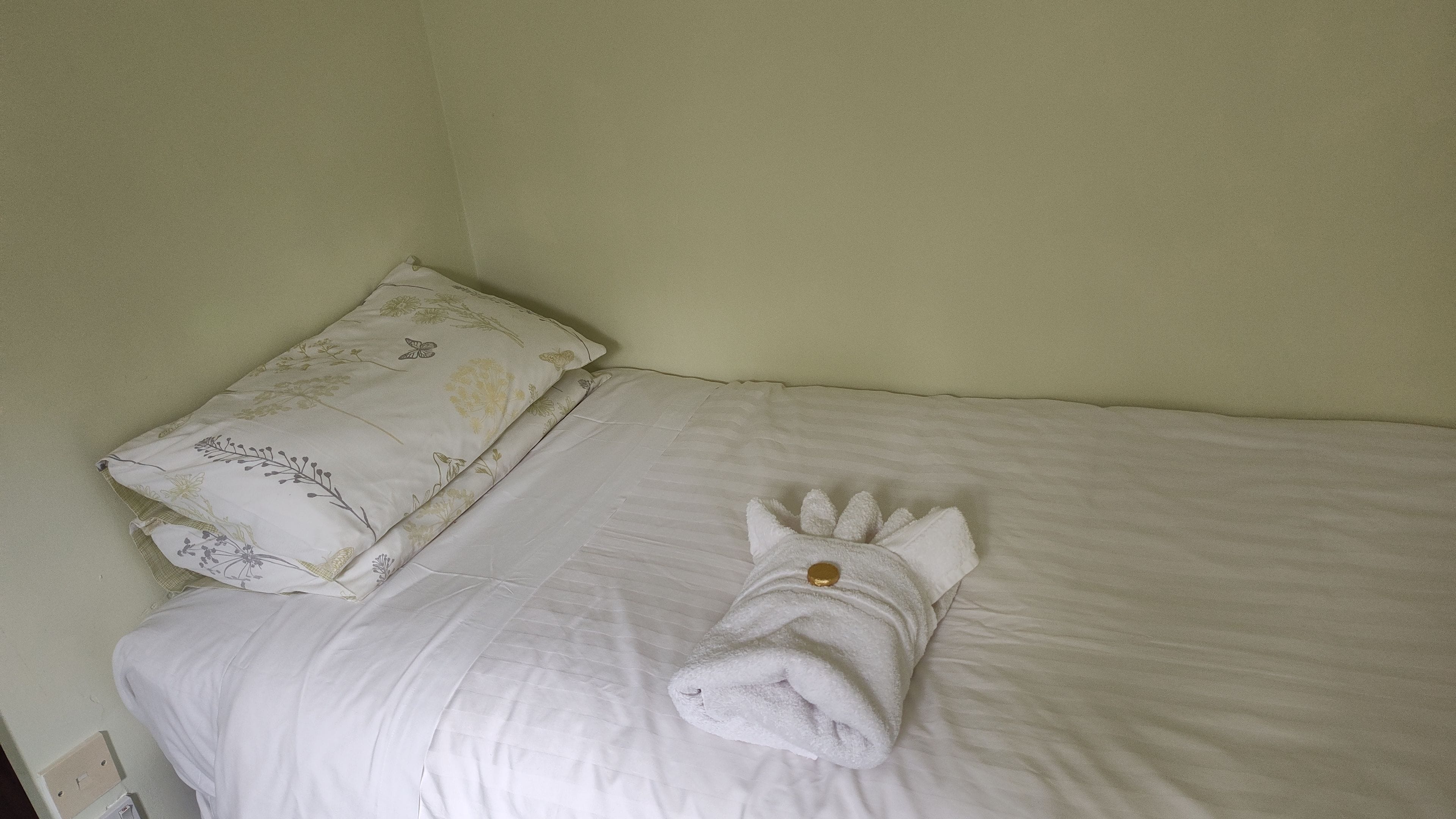 Una cama individual con edredón blanco y almohada estampada.
