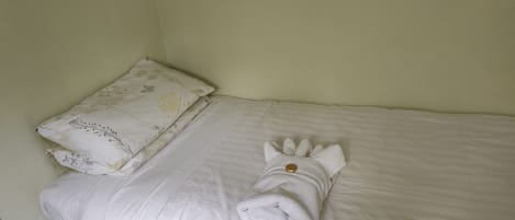 A single bed with a white duvet and a floral pillow.