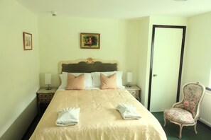 Una habitación de hotel con una cama, dos mesitas de noche, una silla y una puerta.