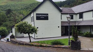 A building with a sign reading 'DOLBRODAETH RIVERSIDE' and a stone wall with a lamp post. - Dolbrodmaeth Riverside  (Machynlleth)