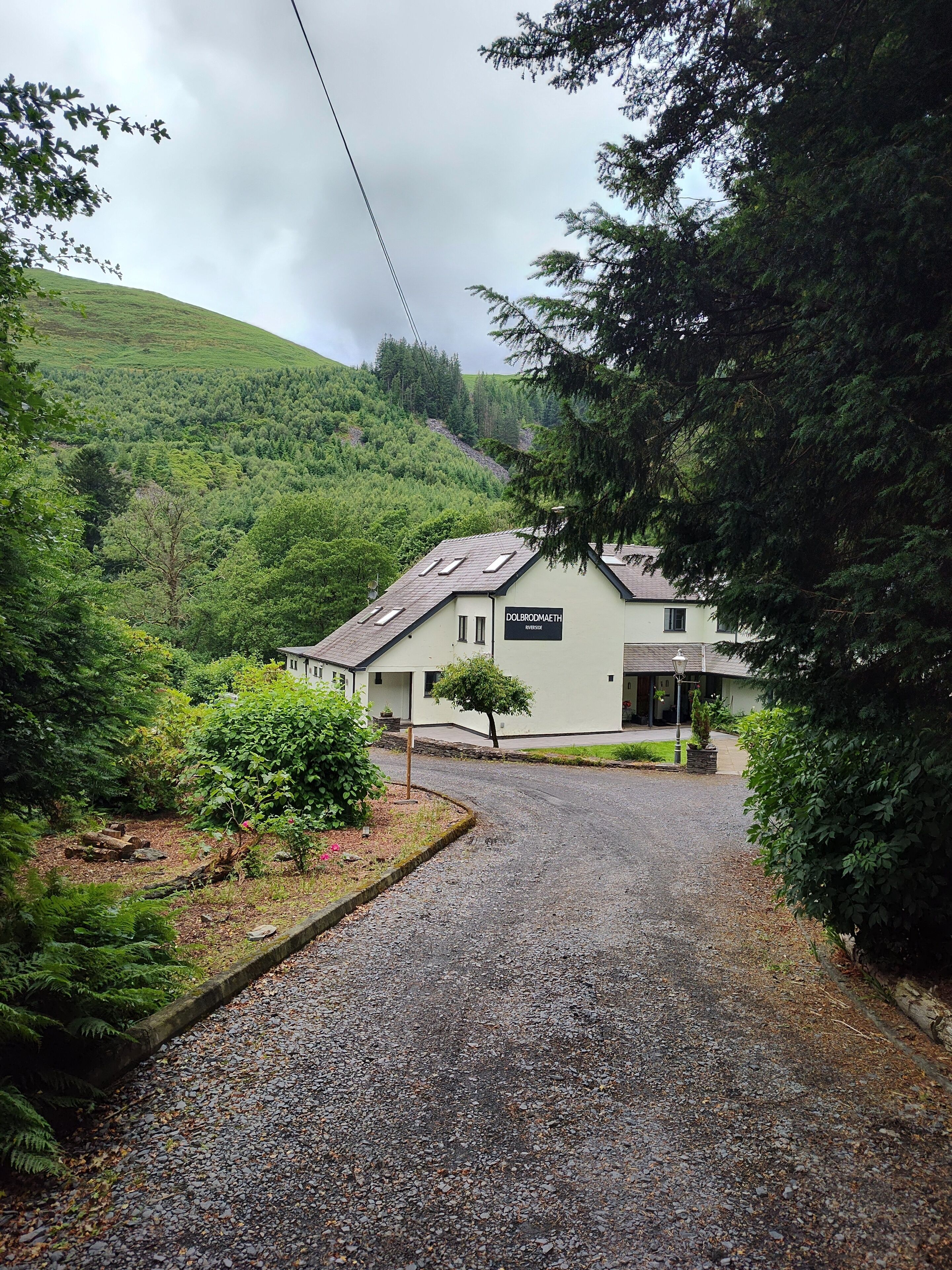 A building with a sign reading 'DOLBRODAETH' in a rural setting with a gravel driveway leading to the entrance.