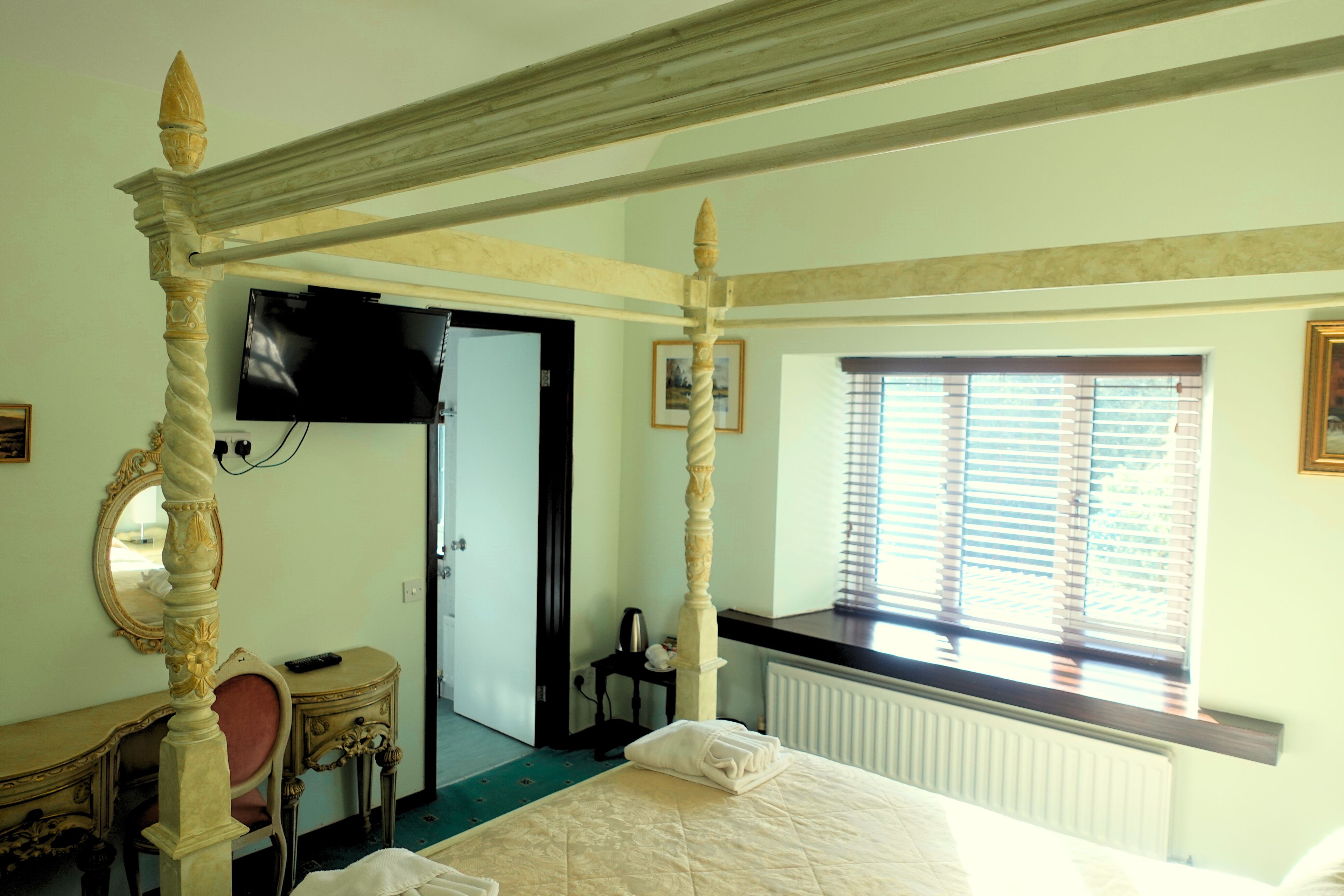 Un dormitorio con cama con dosel, un escritorio con silla, un televisor y una ventana con persianas.