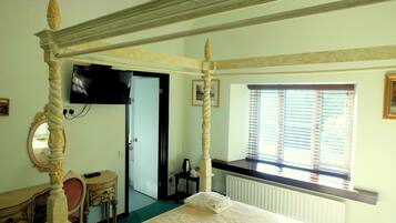Un dormitorio con cama con dosel, un escritorio con silla, un televisor y una ventana con persianas.