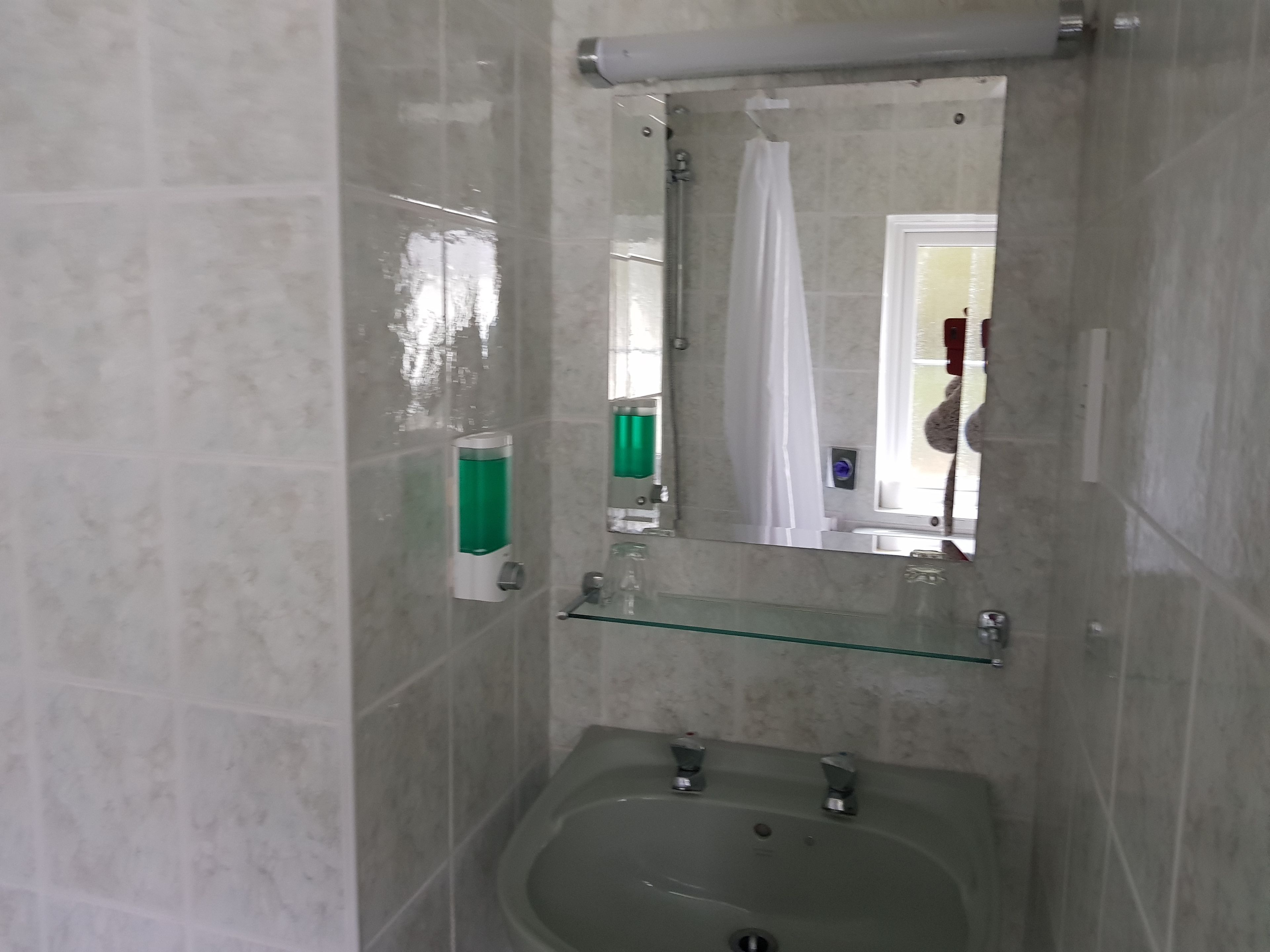 A bathroom with a bathtub, a sink, a mirror, and a glass shelf.