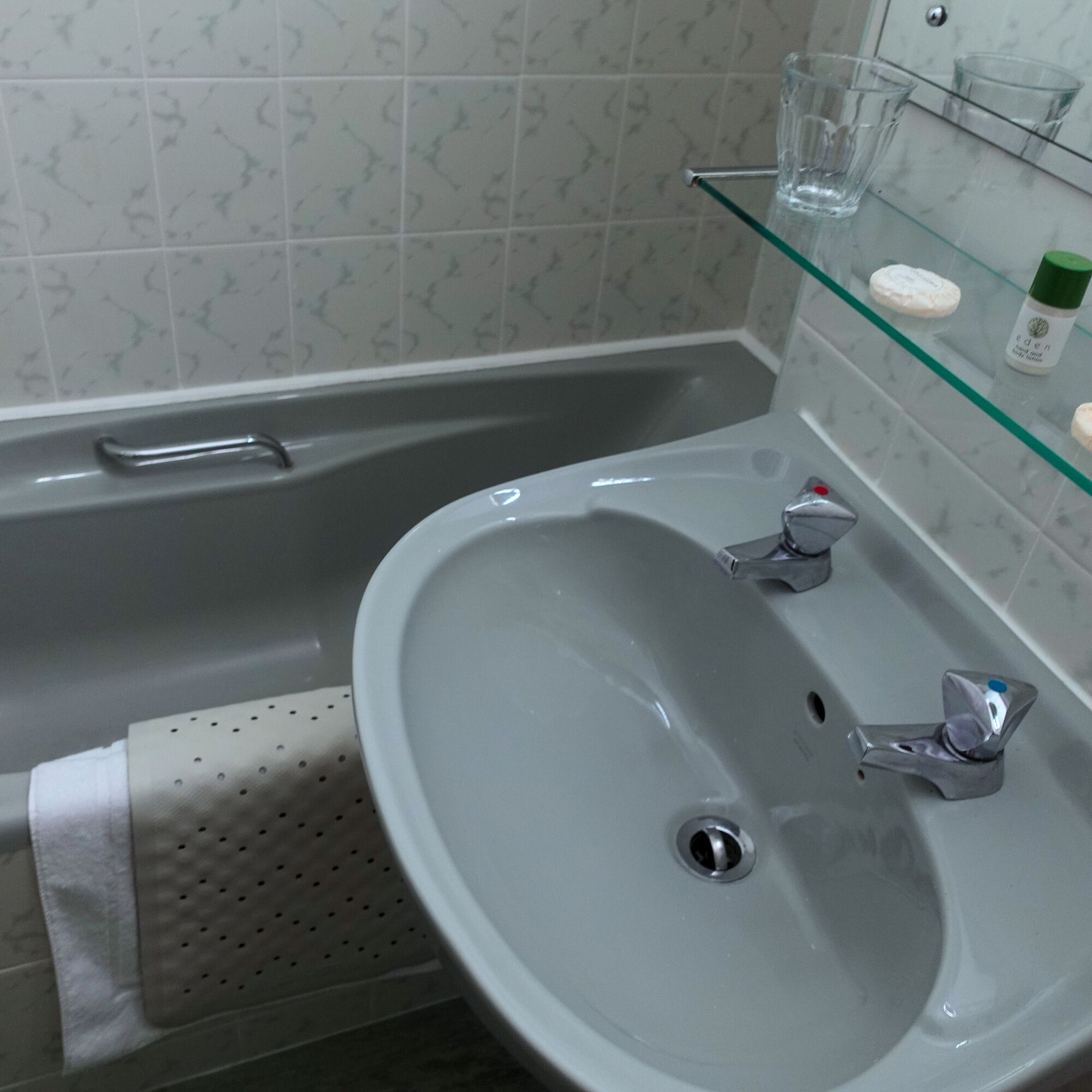 Une salle de bain avec un lavabo gris, une étagère en verre où sont rangés les articles de toilette et un porte-serviettes.
