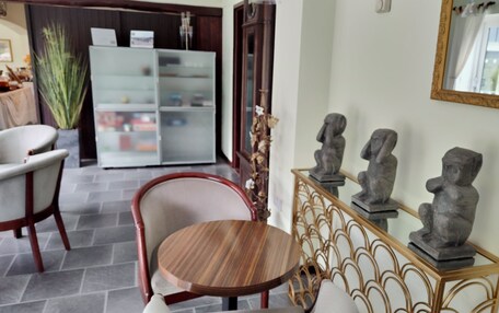 A dining area with a round wooden table and chairs, a glass cabinet with decorative items, and a wall-mounted mirror.