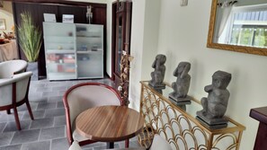 Un comedor con una mesa redonda de madera y sillas, un aparador de vidrio con adornos, y un espejo instalado en la pared.