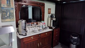 Una kitchenette con cafetera, frascos, tazas y un armario.