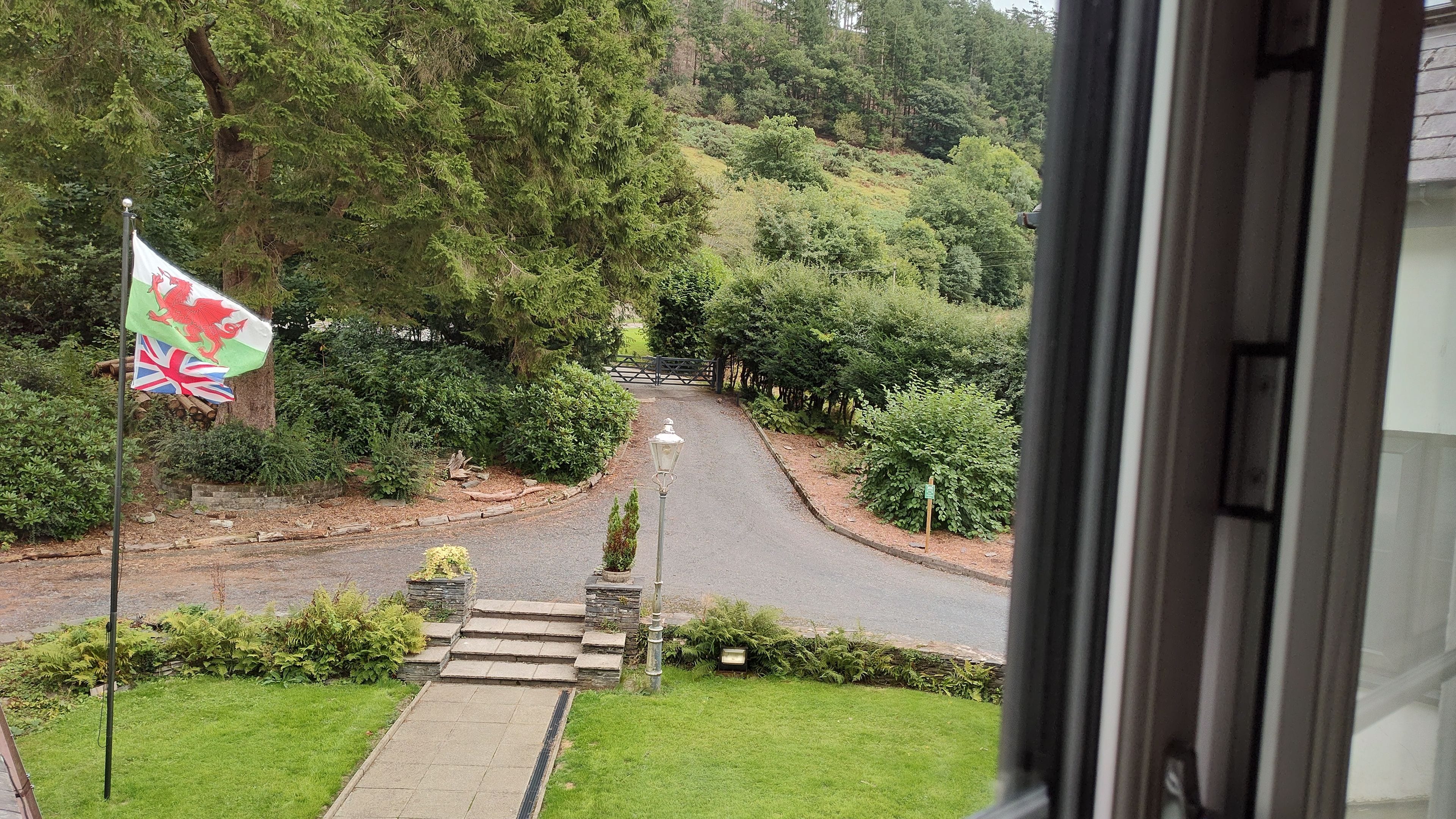 A view of a pathway leading to a gate, surrounded by lush greenery and a flag.