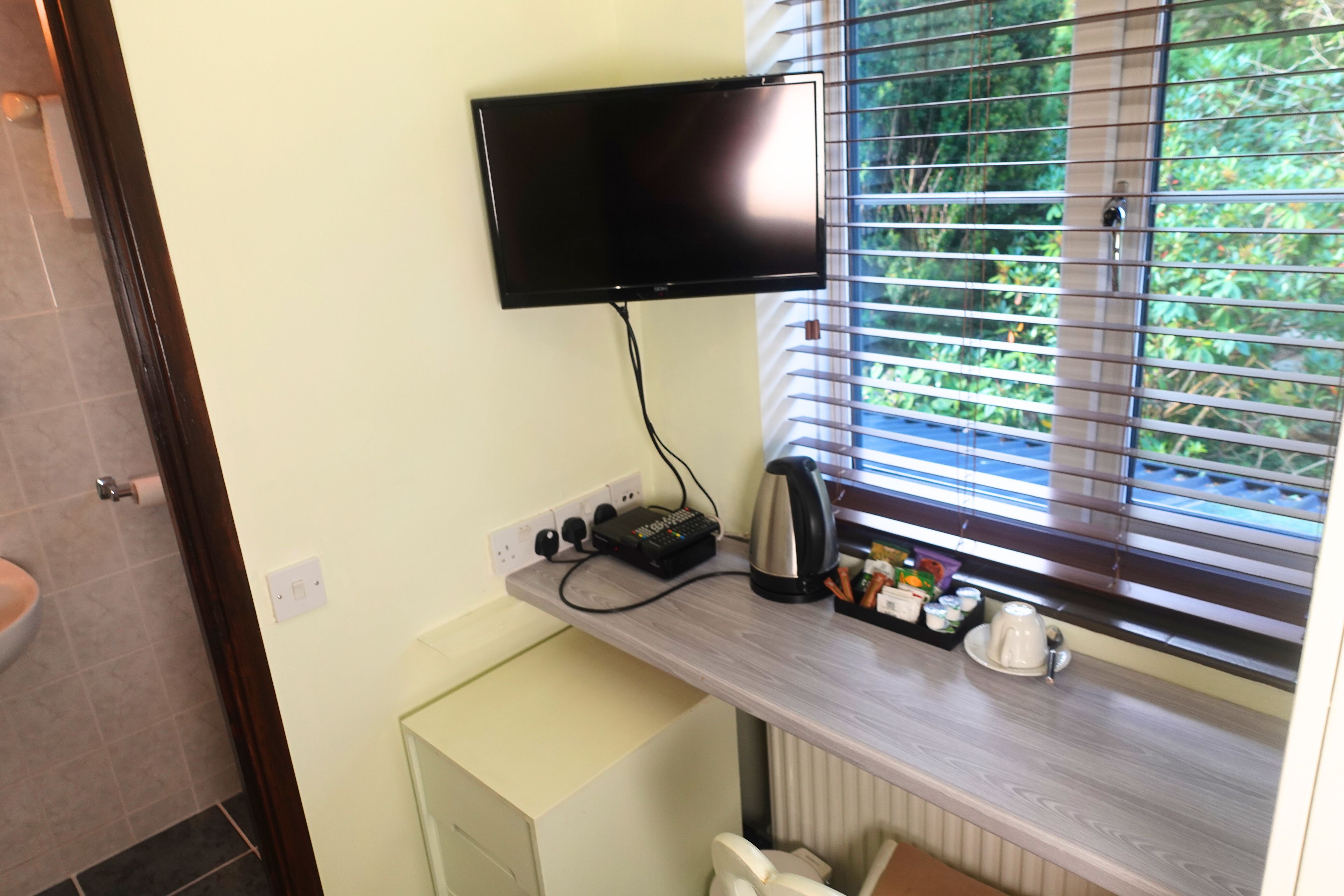 Una pequeña cocina equipada con una televisión de pantalla plana en la pared, una tetera, una cafetera y un mueble pequeño.