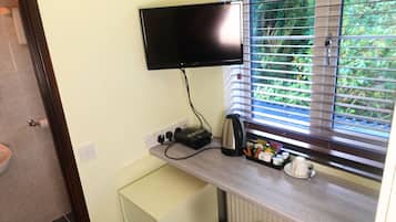 Una pequeña cocina equipada con una televisión de pantalla plana en la pared, una tetera, una cafetera y un mueble pequeño.