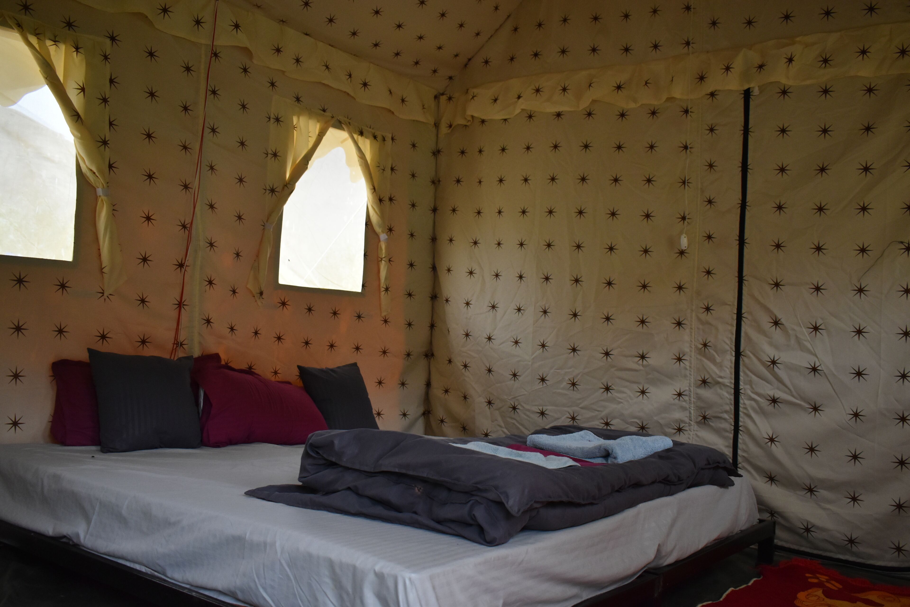 Ein Einzelbett mit weißer Bettdecke, mehreren Kissen und einer Decke in einem zeltähnlichen Raum mit sternenmusterigen Wänden und einem Fenster.
