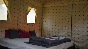 Una cama individual con sábana blanca, múltiples almohadas y una colcha en una habitación tipo tienda con paredes de diseño de estrellas y una ventana.