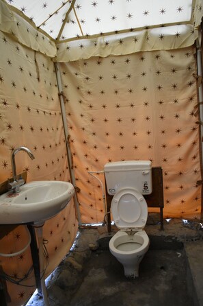 Un baño con carpa que incluye inodoro, lavamanos y tubería de agua.