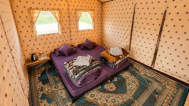 Una habitación con carpa, una cama, almohadas, una mesa con hervidor y piso estampado.