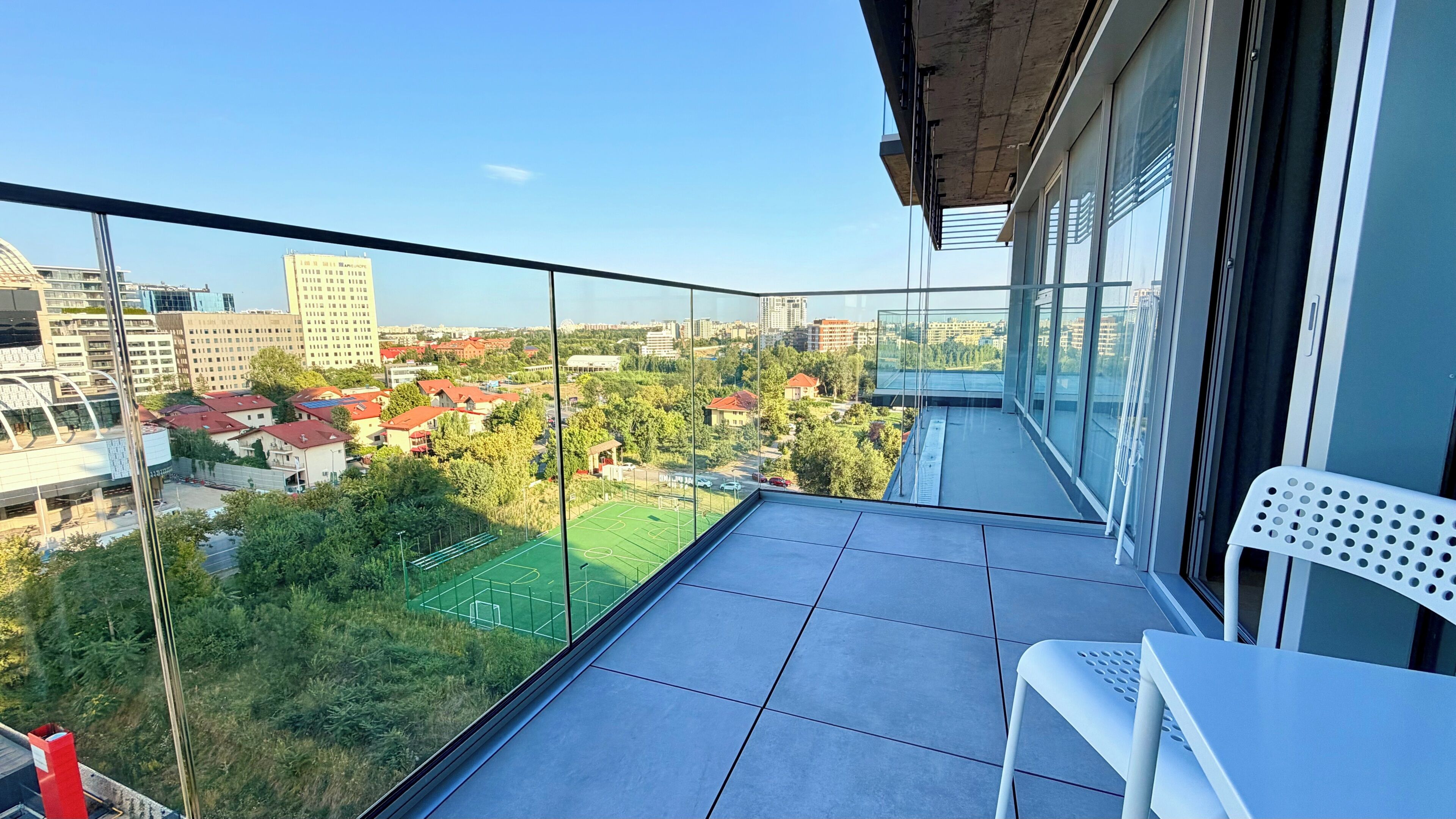 Un balcón con vista despejada a un campo deportivo y edificios circundantes.