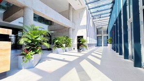 Espacio interior moderno con área central abierta, rodeado de paredes con ventanales amplios y plantas en macetas.