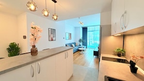 Una cocina moderna con una isla central, luces colgantes y vistas a una sala de estar con un sofá y una planta.