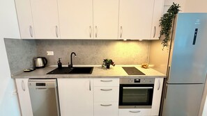 Una cocina moderna con armarios blancos, un lavamanos negro, horno empotrado y un refrigerador de acero inoxidable.