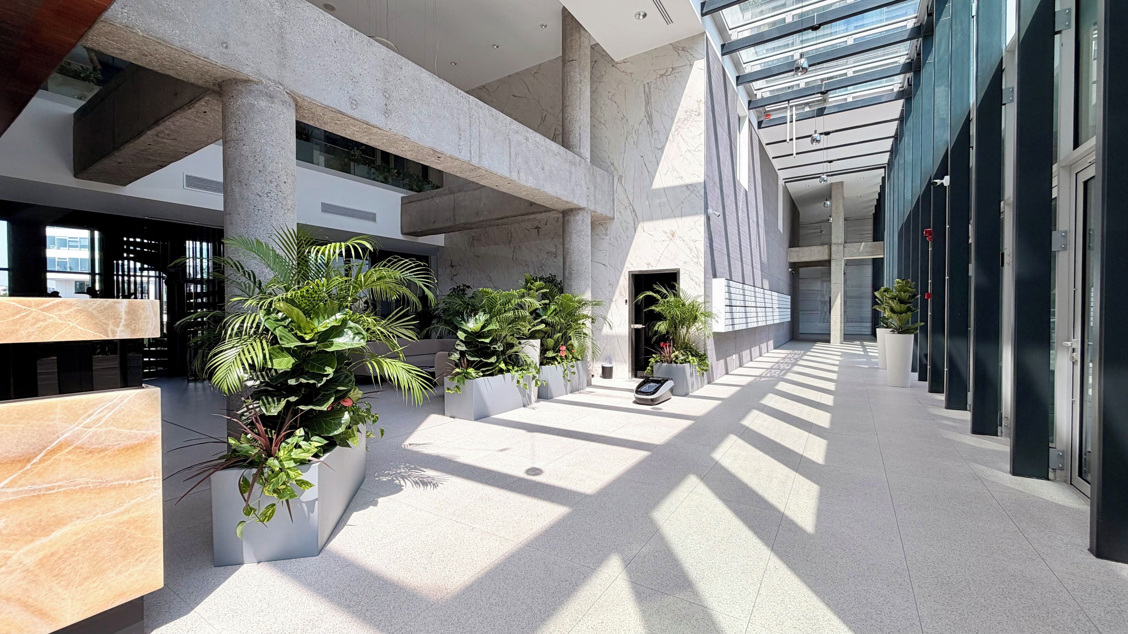 Um espaço interior moderno com área central aberta, rodeado por paredes com grandes janelas e plantas em vasos.