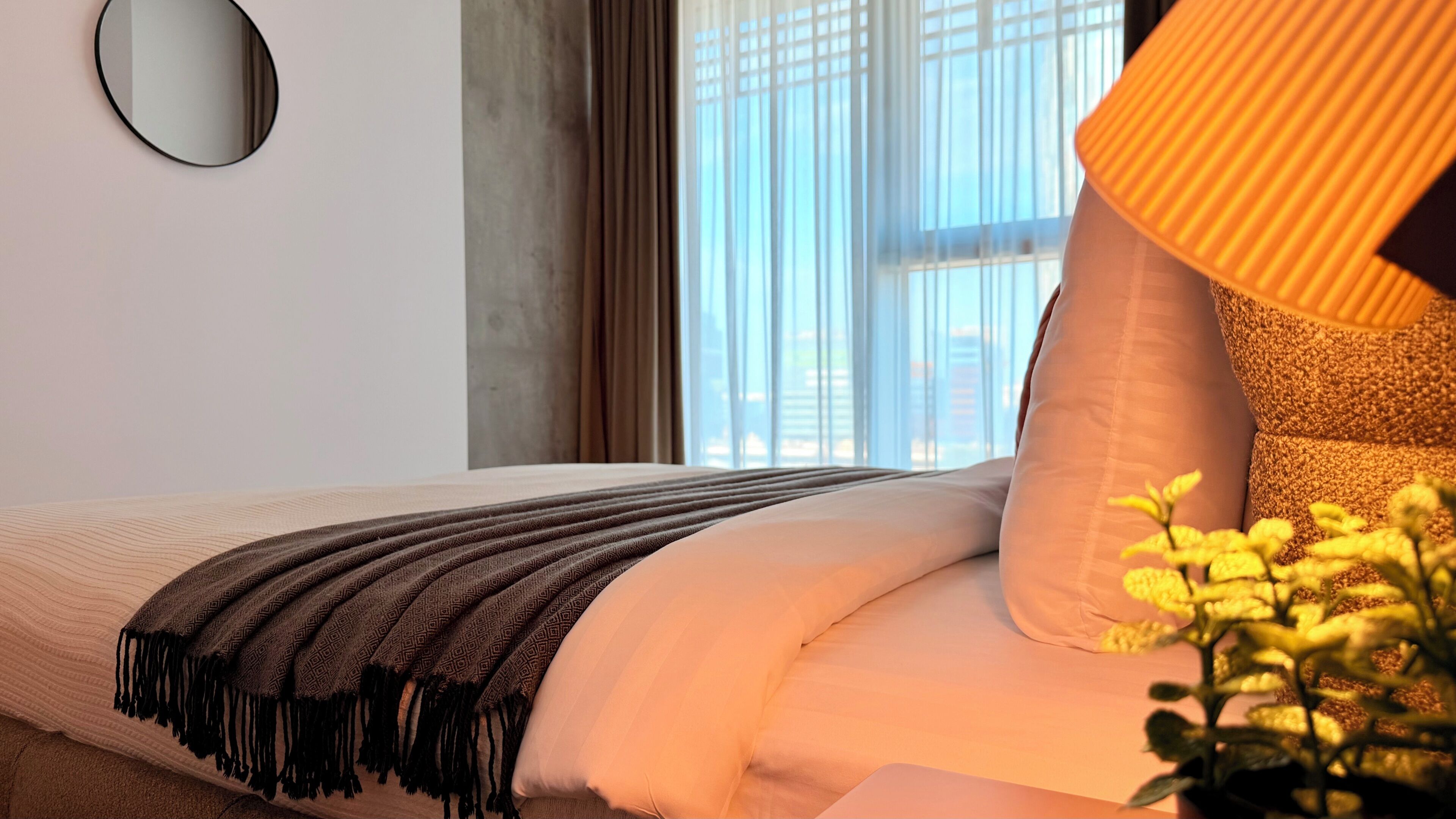 Ein Hotelzimmer mit einem Bett, einem runden Spiegel, einem Fenster mit Vorhängen und einer Lampe.