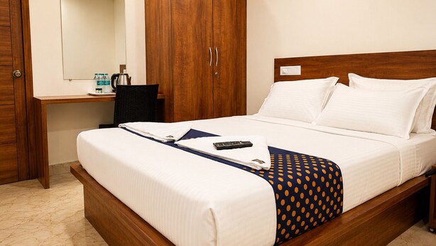 A hotel room with a bed, a wooden wardrobe, a desk with a chair, and a mirror.