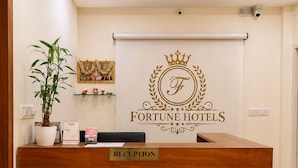 A reception desk with a 'RECEPTION' sign, a potted plant, a calendar, and a framed picture on the wall.