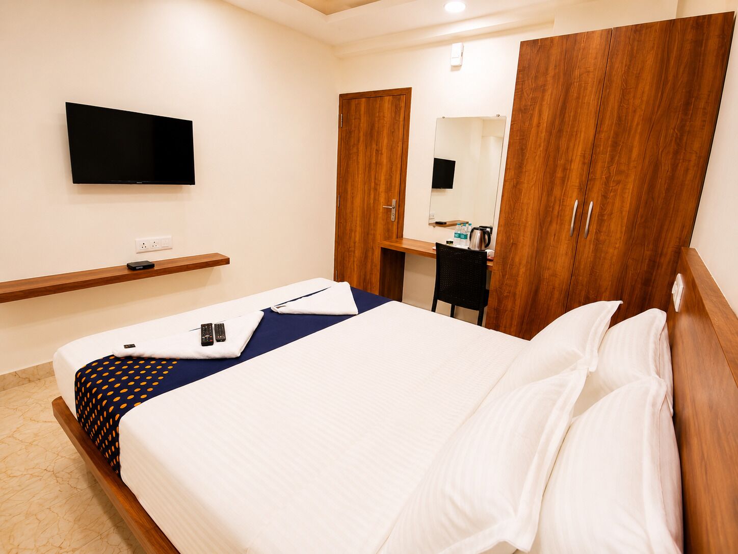 Ein Hotelzimmer mit Bett, Schreibtisch, Stuhl, an der Wand montiertem Fernseher und Holzschränken.