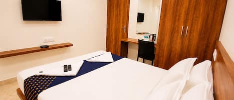 A hotel room with a bed, a desk, a chair, a TV mounted on the wall, and wooden wardrobes.