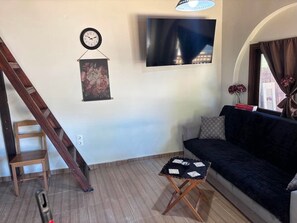 A living room with a sofa, a TV mounted on the wall, a wooden ladder, and a small table with playing cards. - Papyrise Nest (Heraklion)
