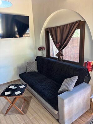 A living room with a dark sofa, patterned cushions, a small wooden table, and a TV mounted on the wall. - Papyrise Nest (Heraklion)