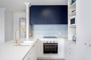 A modern kitchen with white cabinetry, a stainless steel oven, and a blue backsplash. - Ocean Vista On Alex Unit 4 (Alexandra Headland)
