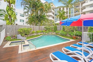 A swimming pool with a wooden deck, lounge chairs, and a stone wall. - Ocean Vista On Alex Unit 4 (Alexandra Headland)