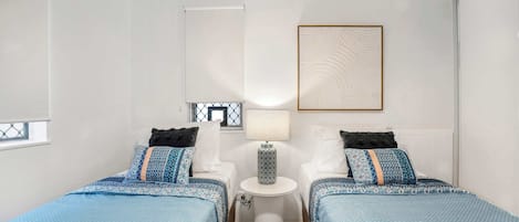 Una camera d'albergo con due letti, un tavolino, una lampada e un quadro appeso al muro.