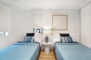 A hotel room with two beds, a small table, a lamp, and a framed picture on the wall. - Ocean Vista On Alex Unit 4 (Alexandra Headland)