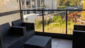 Uma varanda com mobiliário de vime, vista para um edifício e uma área de estacionamento.
