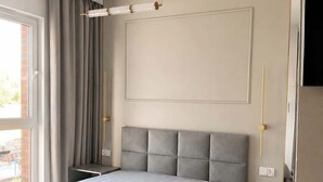 Quarto moderno com uma cama grande, uma mesa de cabeceira, um radiador e uma janela com cortinas.