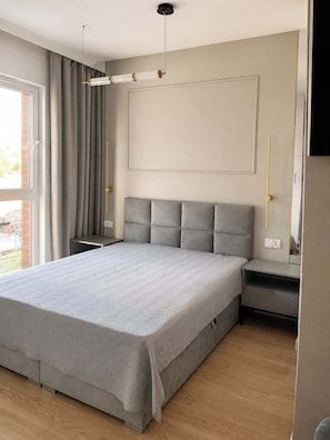 Ein modernes Schlafzimmer mit einem großen Bett, einem Nachttisch, einem Heizkörper und einem Fenster mit Vorhängen.