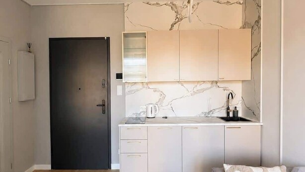 A modern kitchen with marble backsplash, a dark door, and a light-colored sofa with patterned cushions.