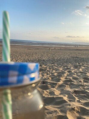 A beach scene with a blurred foreground object, possibly a bottle or container, and a clear view of the sandy beach and distant shoreline.
