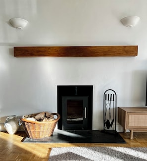A modern living room with a fireplace, a wooden shelf above it, a wicker basket, and a decorative metal piece.