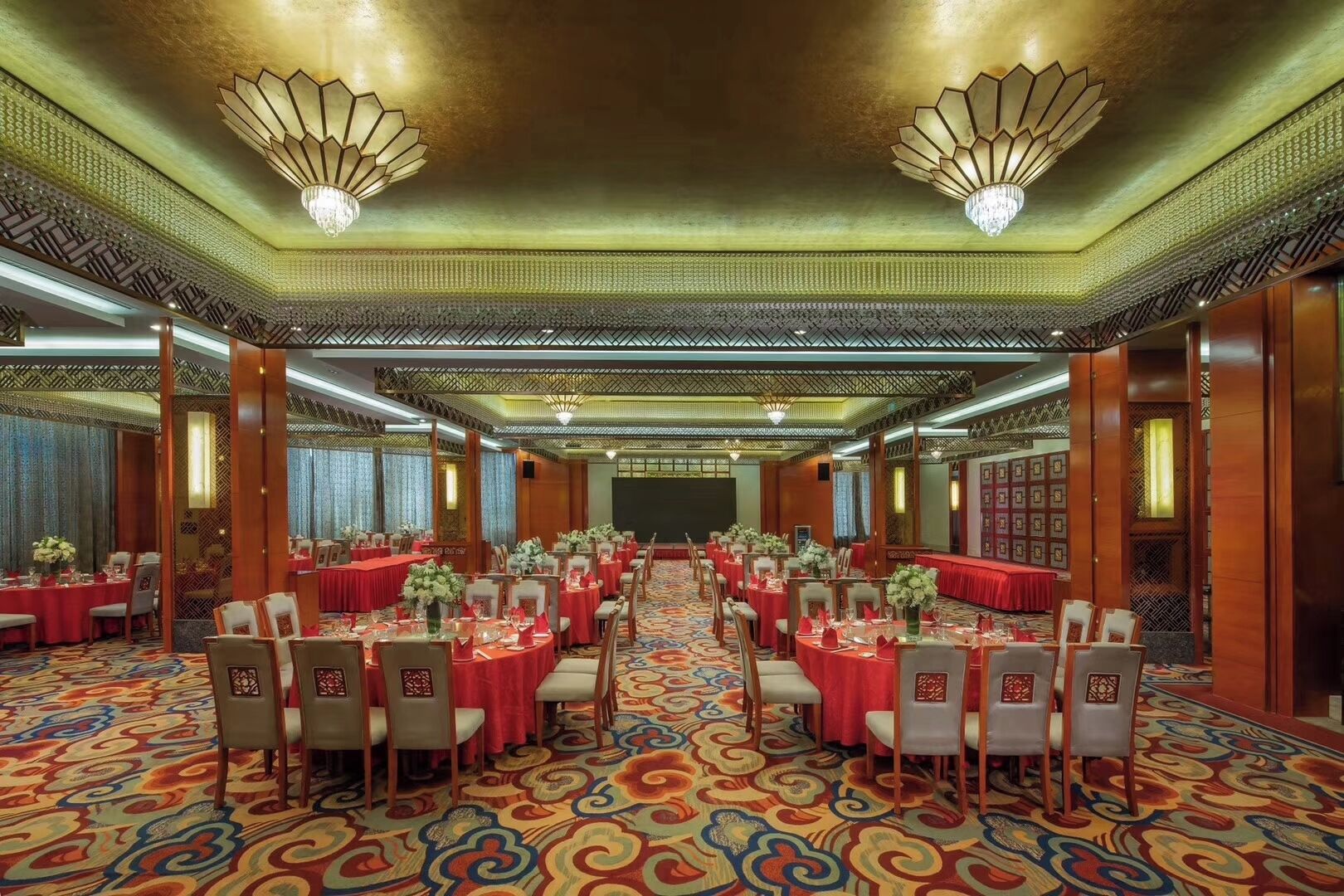 A banquet hall with round tables, chairs, and a patterned carpet.